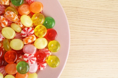 Plate with delicious colorful candies on wooden table, top view. Space for text