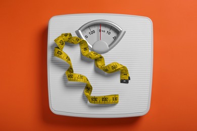 Photo of Scales and measuring tape on orange background, top view. Weight loss concept