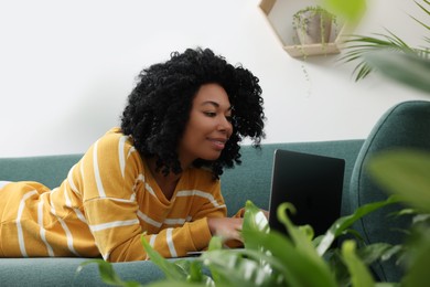 Photo of Relaxing atmosphere. Woman with laptop lying on sofa near houseplants indoors