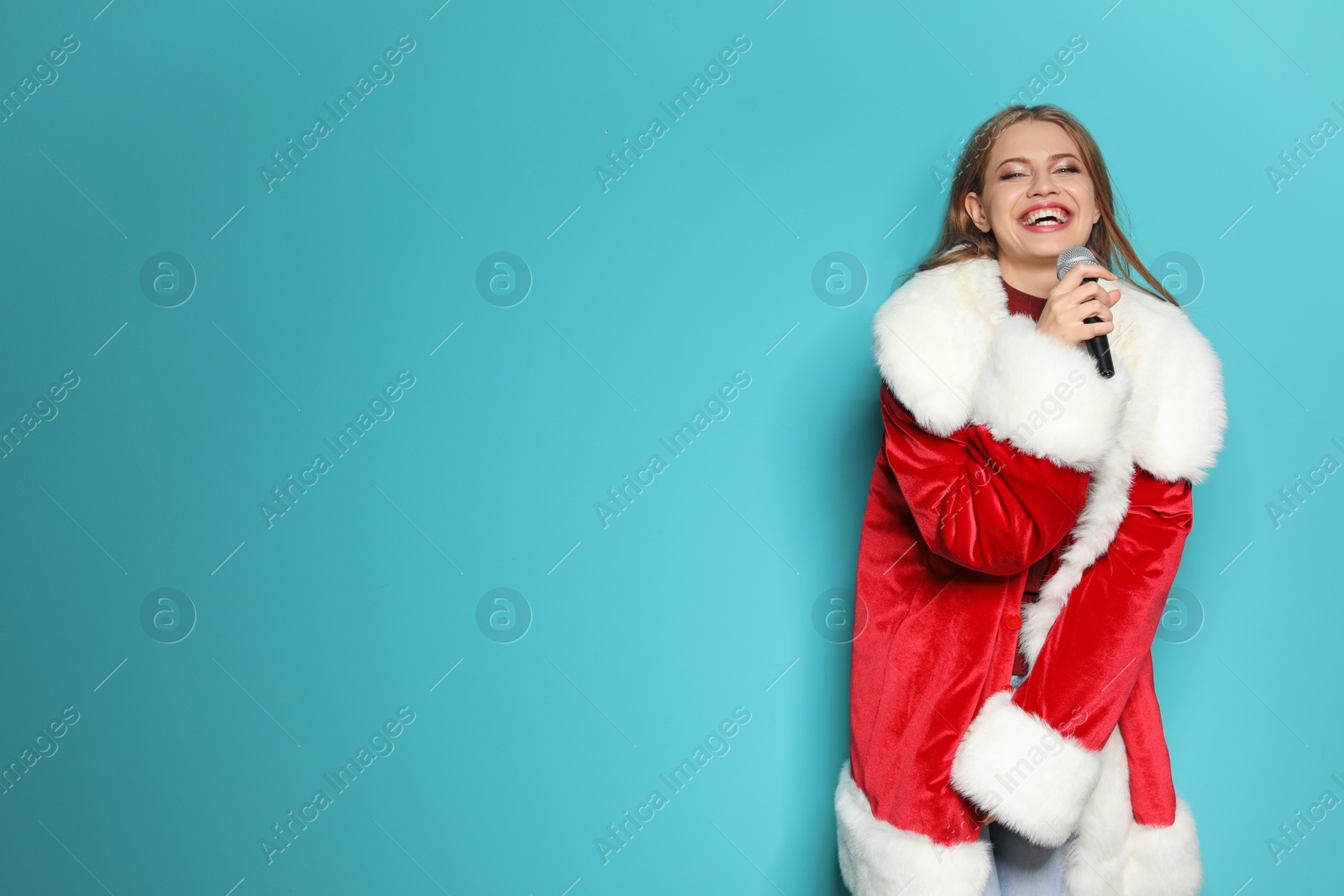 Photo of Young woman in Santa costume singing into microphone on color background. Christmas music