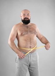 Fat man with measuring tape on grey background. Weight loss