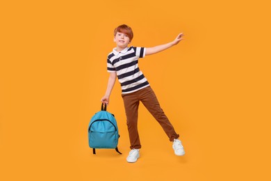 Smiling schoolboy with backpack on orange background