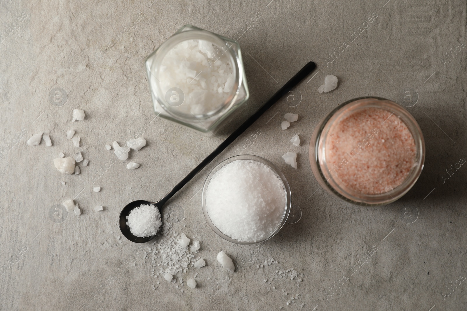 Photo of Different natural salt on grey textured table, flat lay