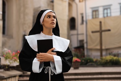 Photo of Young nun with Bible near building outdoors, space for text