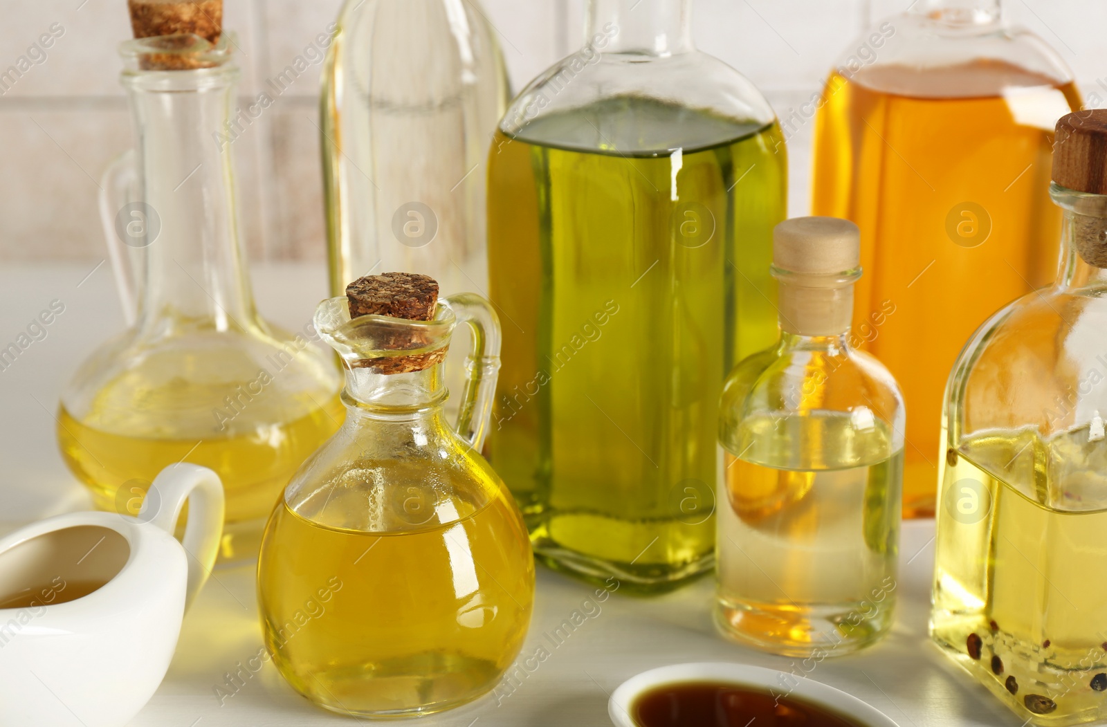 Photo of Vegetable fats. Different oils in glass bottles and dishware on white wooden table, closeup