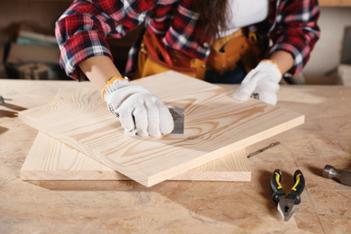 Female carpenter polishing wooden board in workshop, closeup