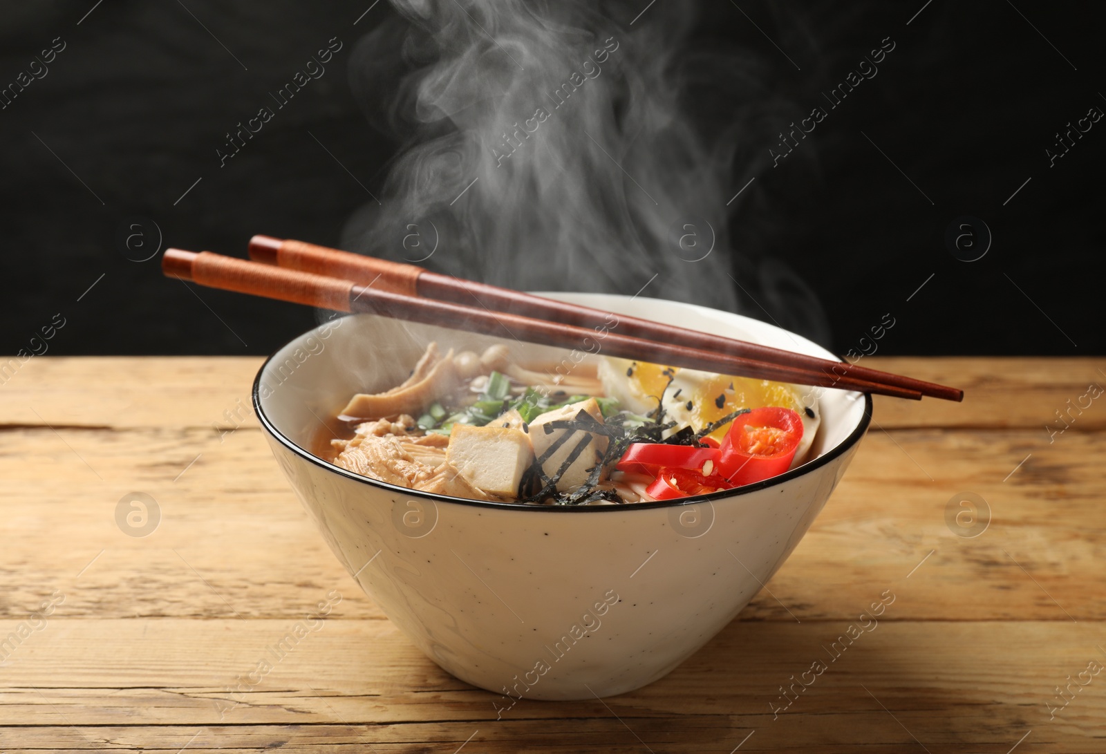 Image of Bowl of hot ramen and chopsticks on wooden table. Noodle soup