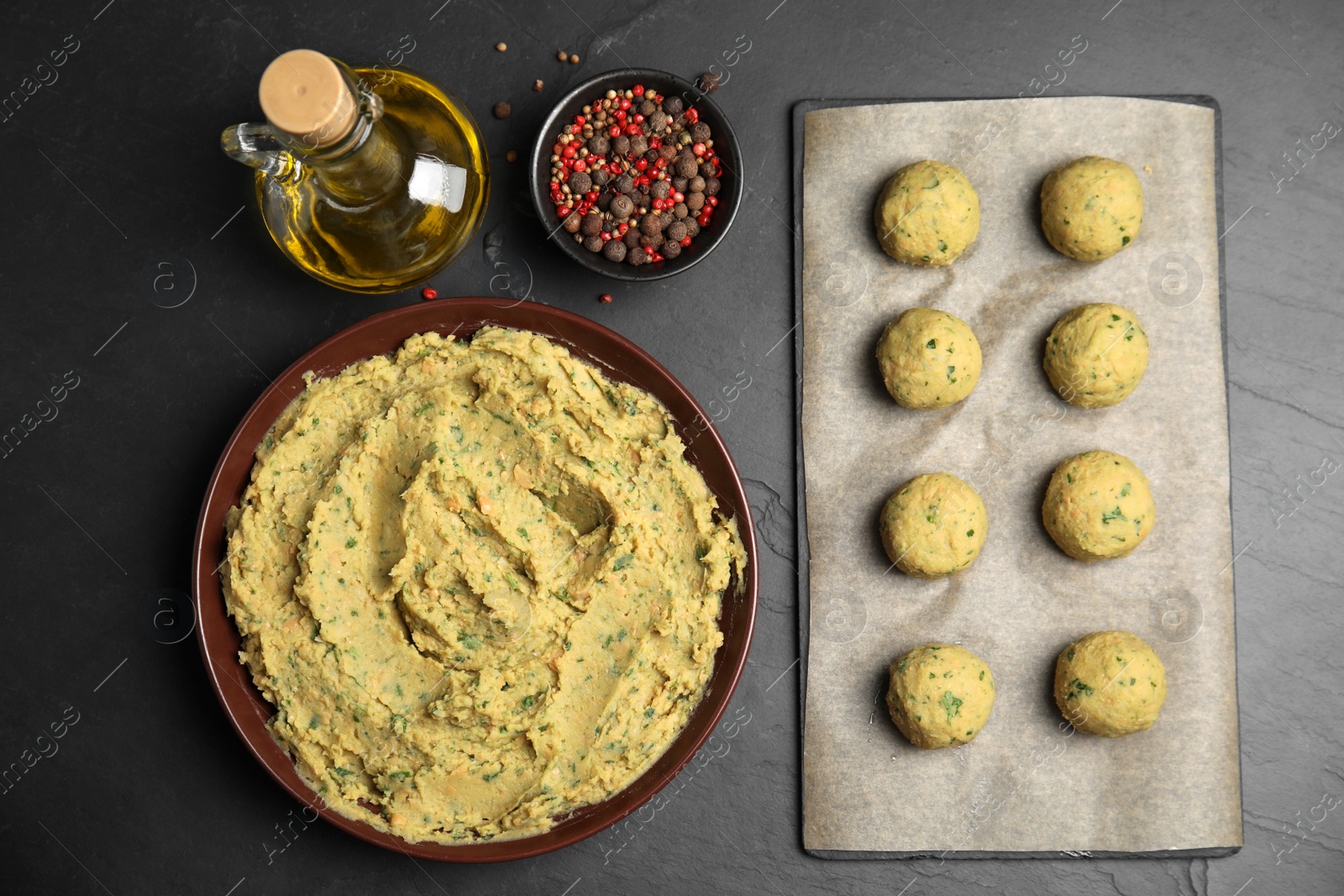 Photo of Raw falafel balls and ingredients on black table, flat lay