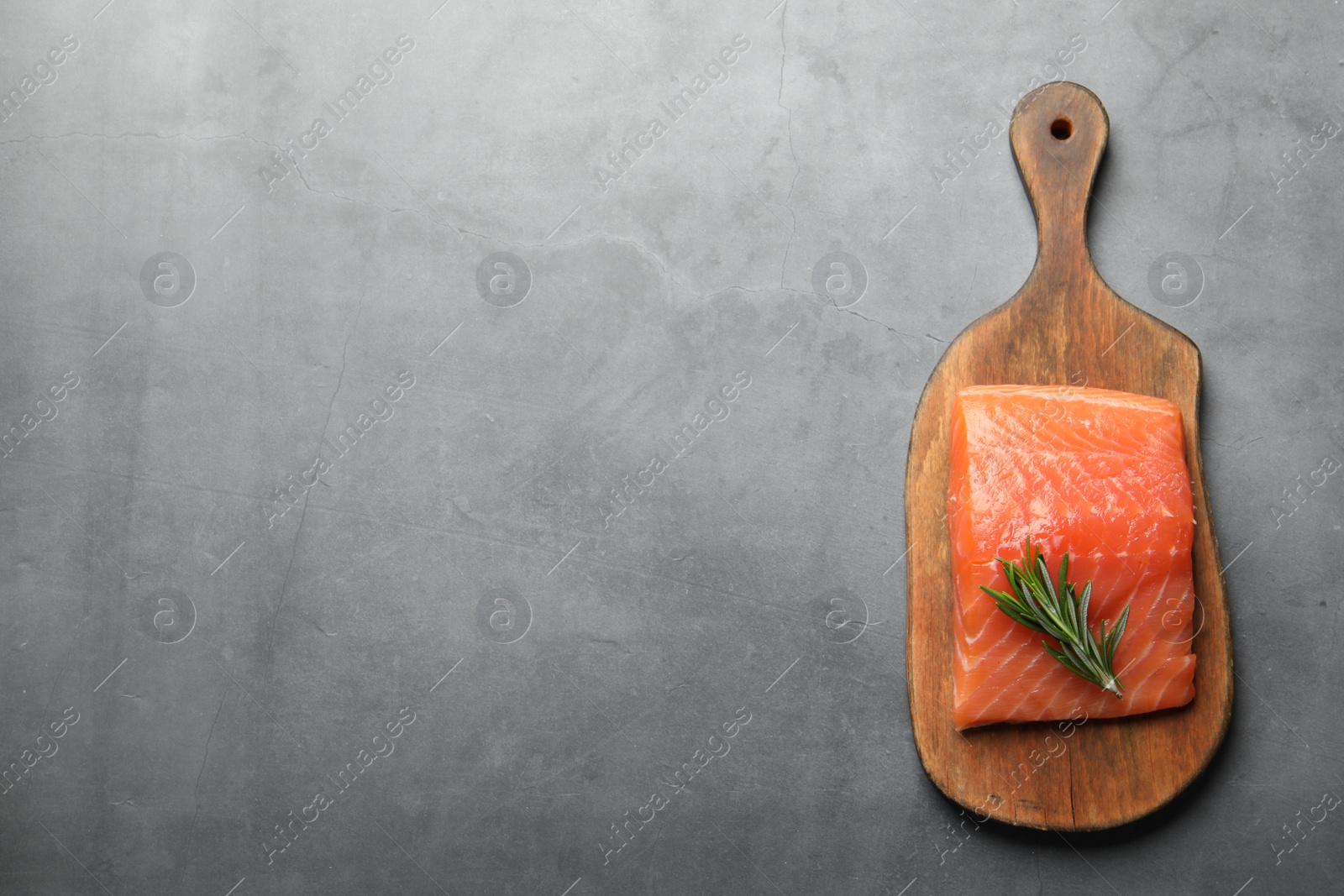 Photo of Fresh raw salmon and rosemary on grey table, top view. Space for text