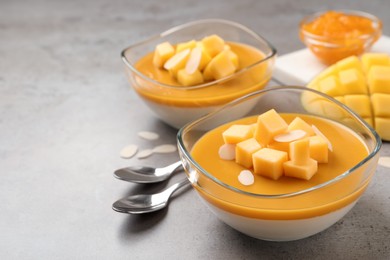 Photo of Delicious panna cotta with mango coulis and fresh fruit pieces on grey table. Space for text
