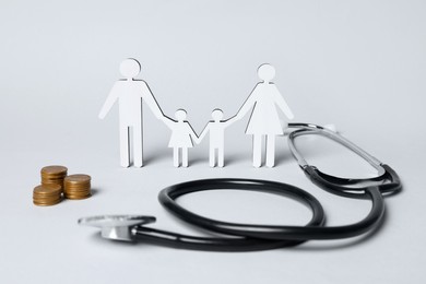 Figures of family stainding near stethoscope and coins on white background. Insurance concept