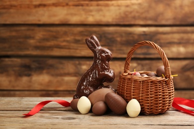 Photo of Sweet chocolate eggs and bunny on wooden table. Space for text