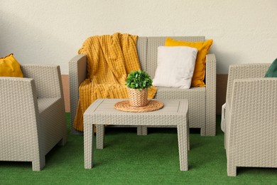 Beautiful rattan garden furniture, soft pillows, blanket and houseplant near white wall