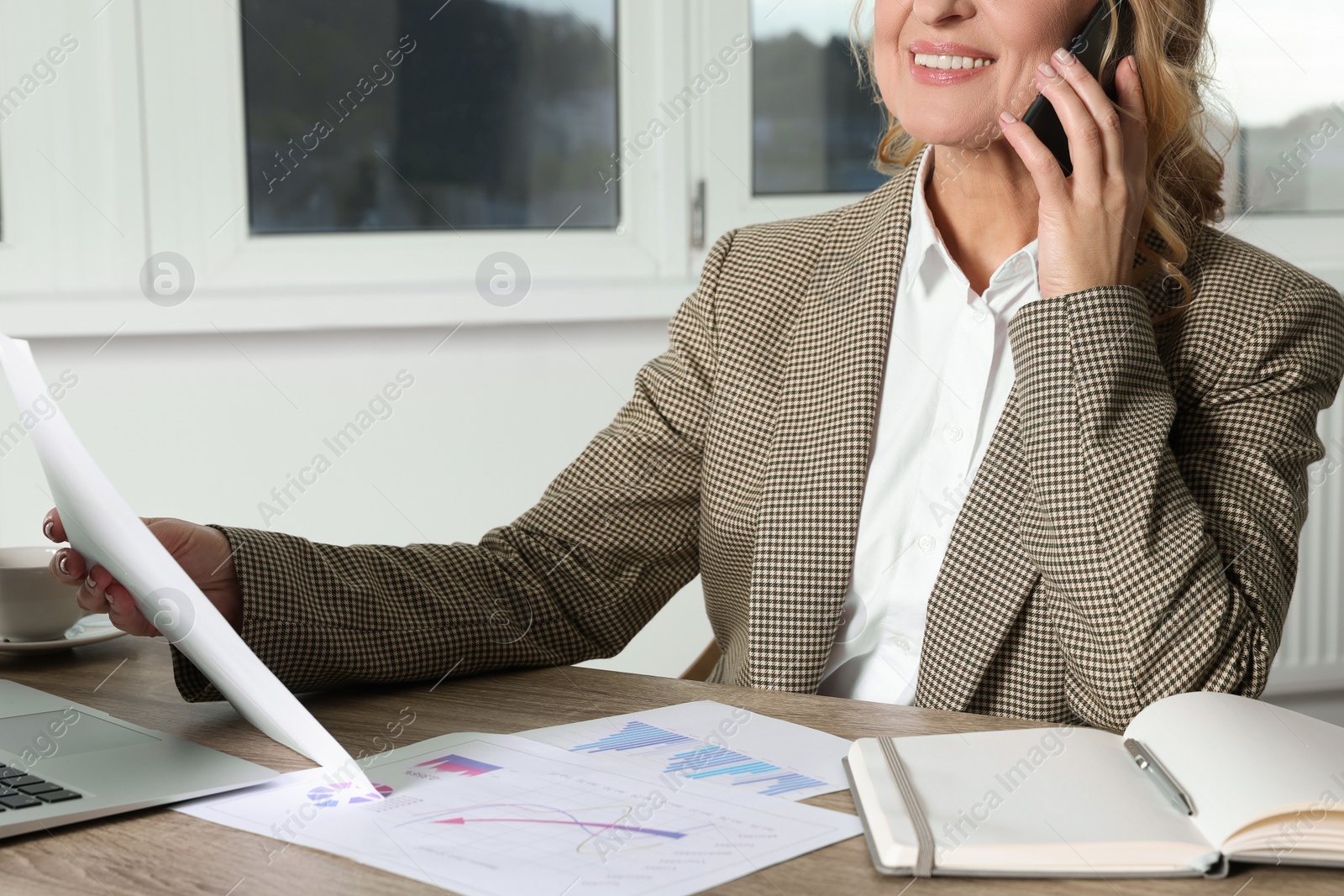 Photo of Lady boss with papers talking on smartphone at desk in office, closeup. Successful businesswoman