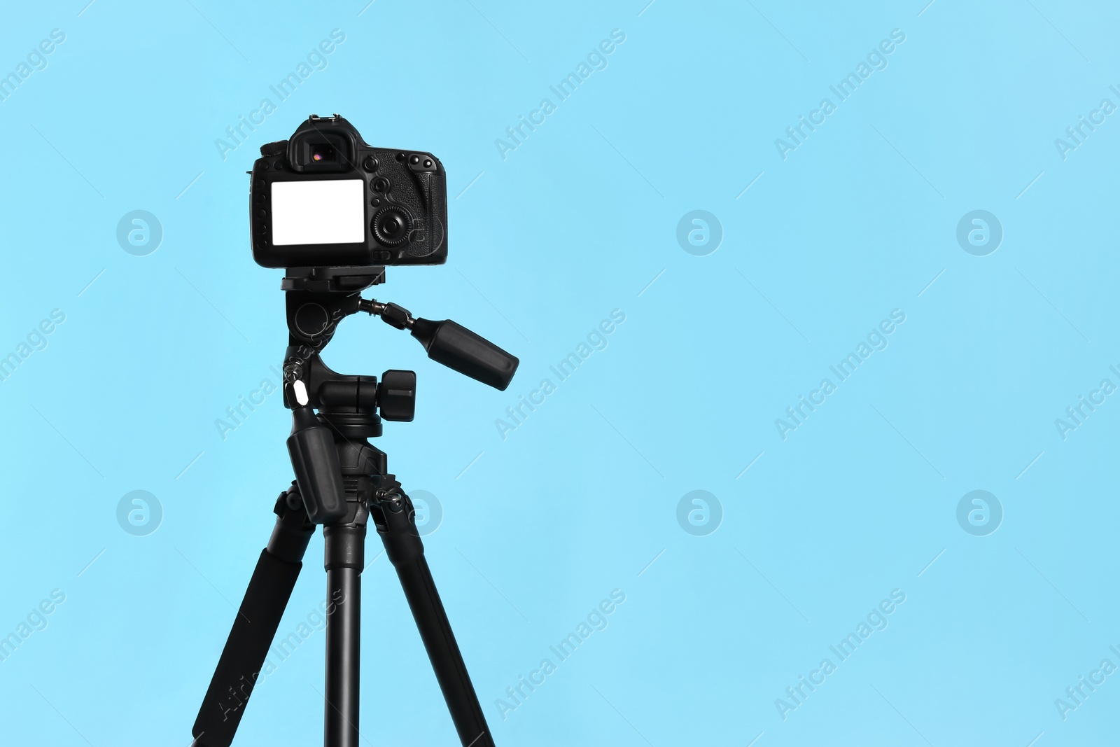 Photo of Modern tripod with professional camera on light blue background. Space for text