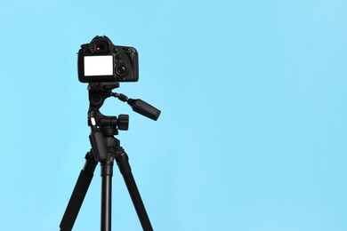 Modern tripod with professional camera on light blue background. Space for text