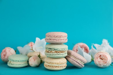 Delicious macarons and flowers on light blue background, space for text