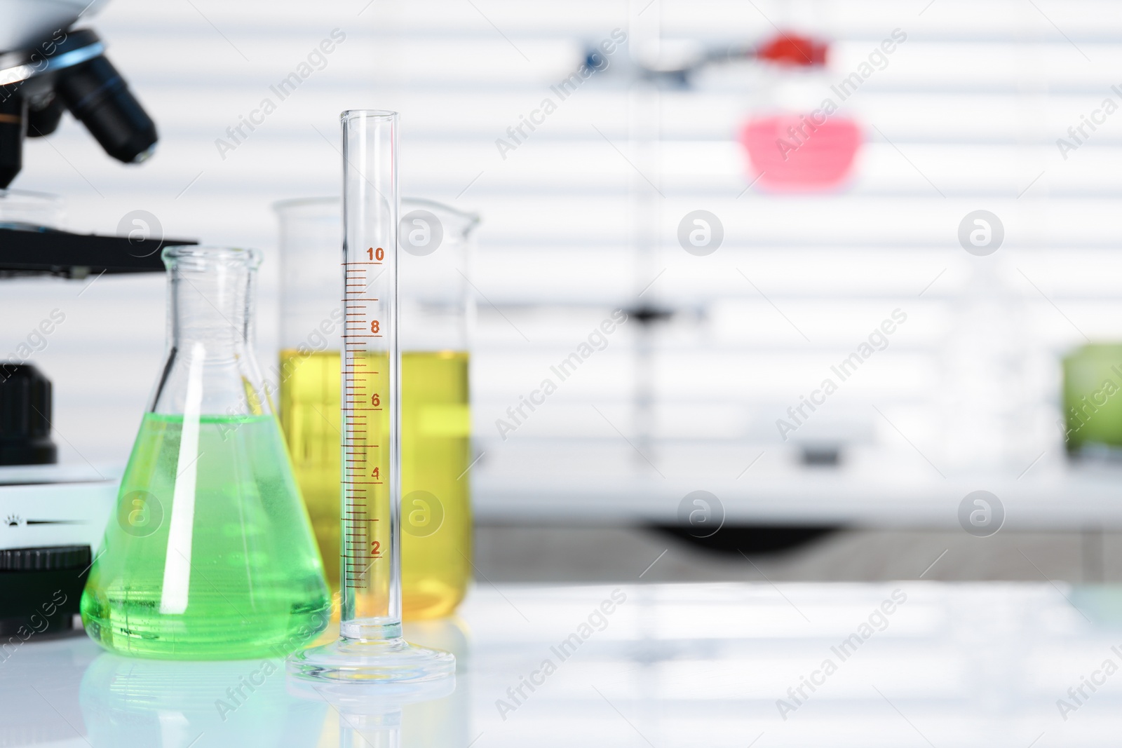 Photo of Laboratory analysis. Different glassware with liquids and microscope on white table indoors, space for text