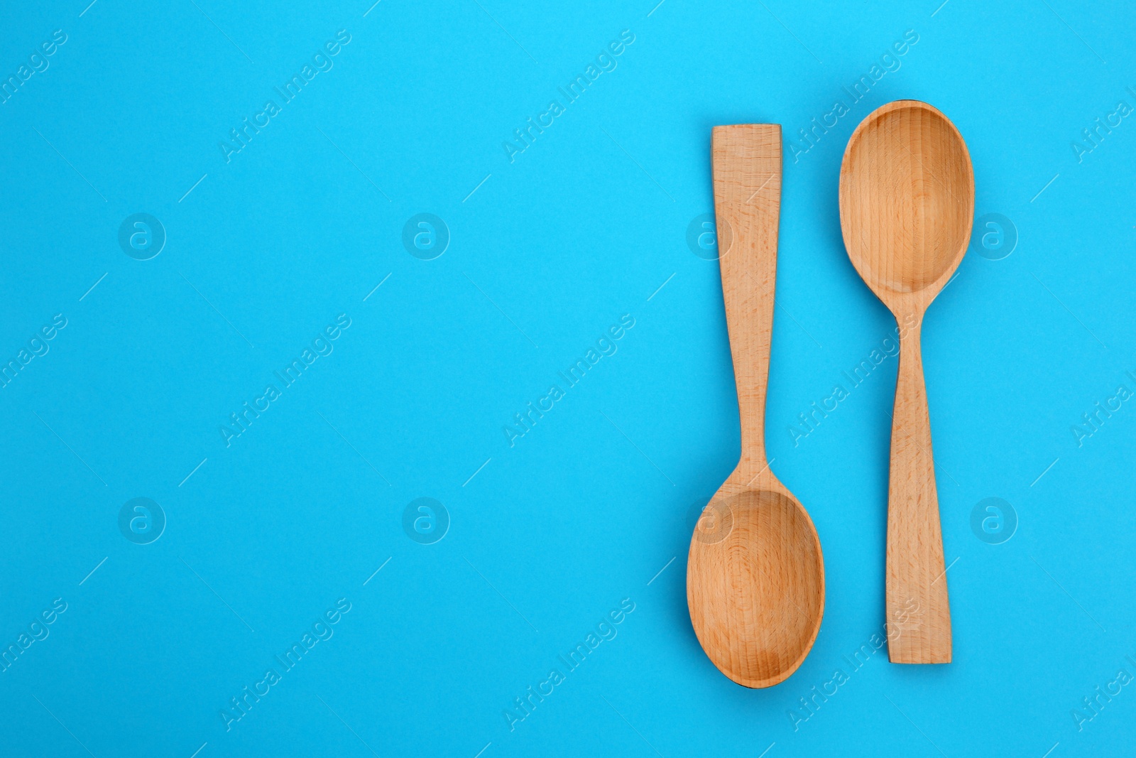 Photo of Clean empty wooden spoons on blue background, flat lay. Space for text