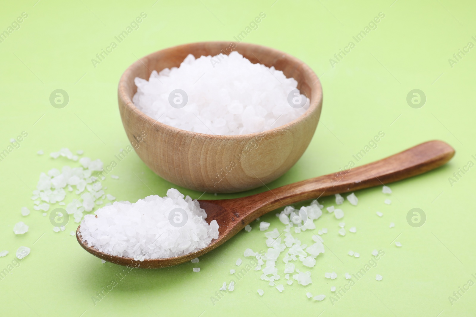 Photo of Bowl and spoon with sea salt on light green background