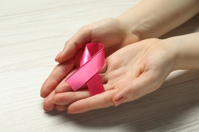 Photo of Breast cancer awareness. Woman with pink ribbon at white wooden table, closeup