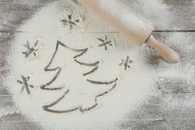 Photo of Christmas tree and snowflakes made of flour near rolling pin on wooden table, top view