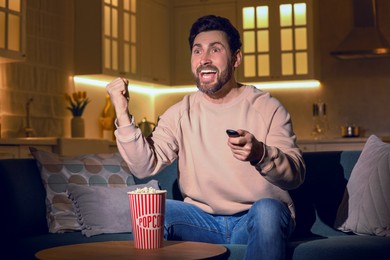 Photo of Excited man watching TV with popcorn on sofa at home