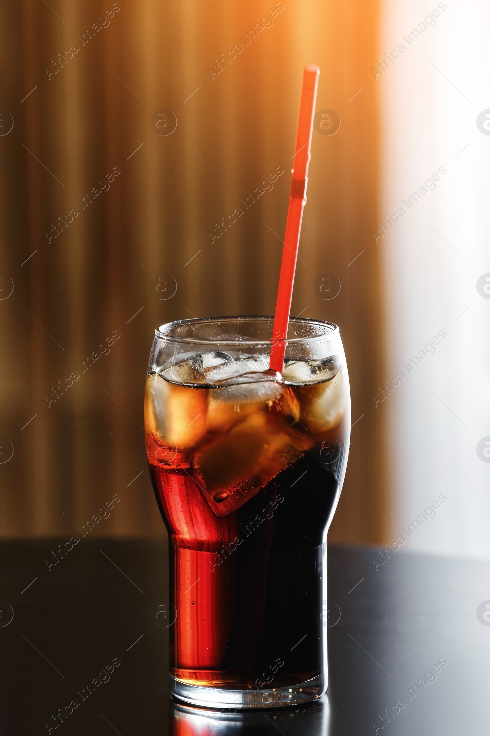 Photo of Glass of cola with ice on table against blurred background