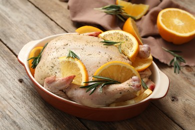 Photo of Chicken with orange slices and rosemary in baking pan on wooden table