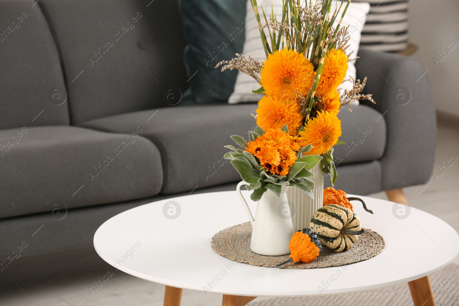 Photo of Beautiful autumn bouquets and pumpkins on coffee table near sofa in room