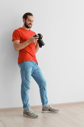 Young photographer with professional camera near white wall