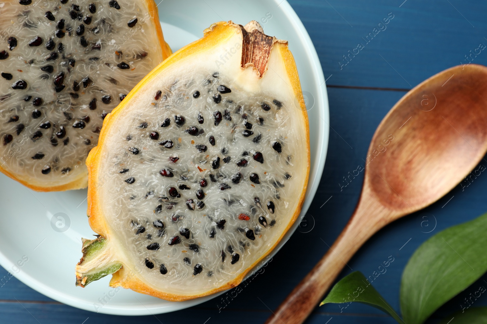 Photo of Plate with delicious cut dragon fruit (pitahaya) and spoon on blue wooden table, flat lay