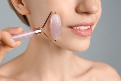 Photo of Young woman using natural rose quartz face roller on light grey background, closeup