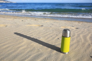 Photo of Yellow thermos with hot drink on sand near sea, space for text