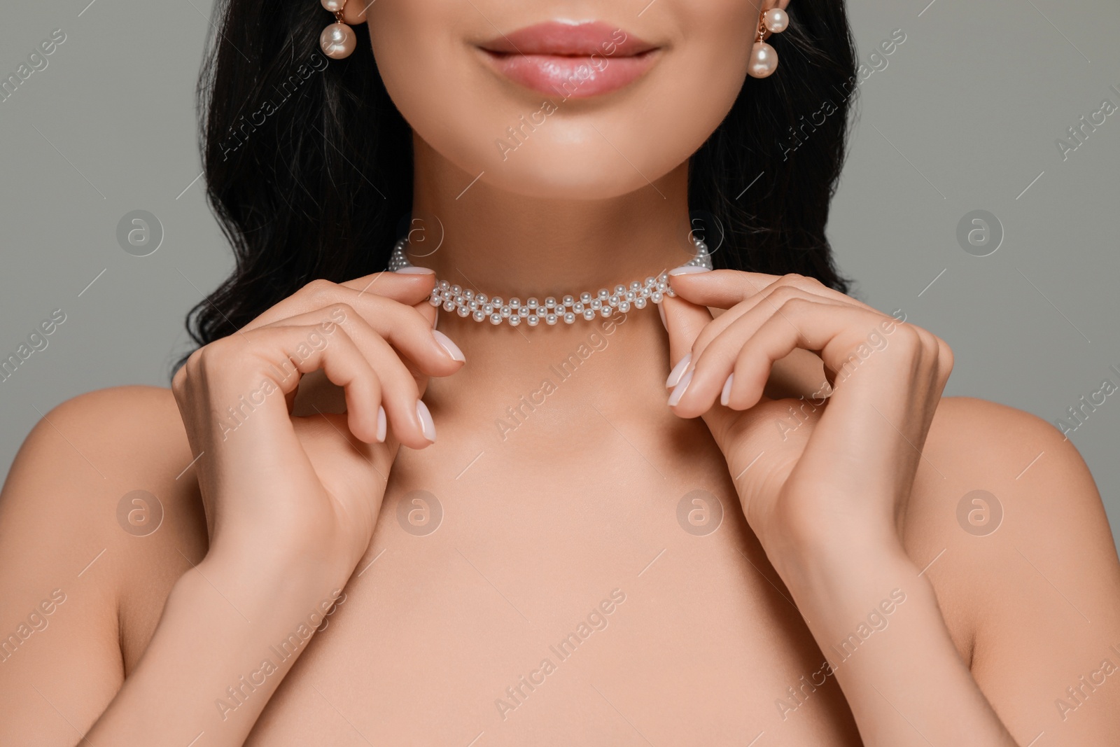 Photo of Young woman wearing elegant pearl jewelry on grey background, closeup