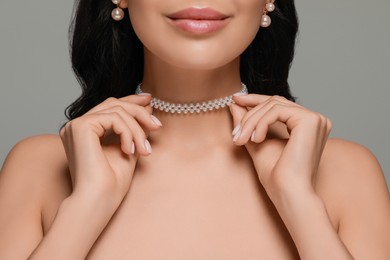 Photo of Young woman wearing elegant pearl jewelry on grey background, closeup