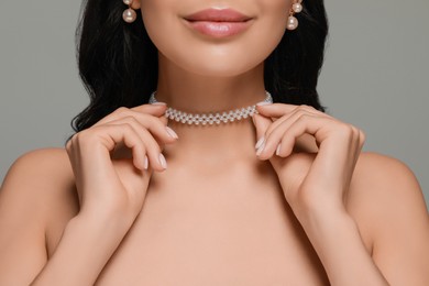 Young woman wearing elegant pearl jewelry on grey background, closeup