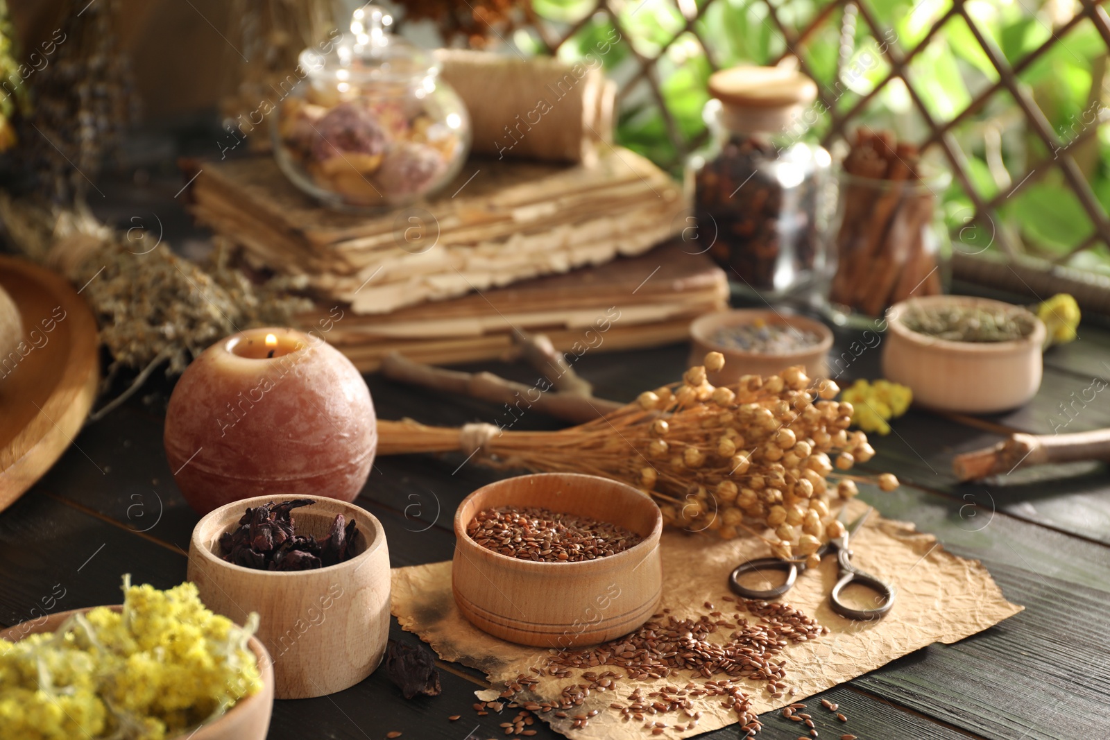 Photo of Different dry herbs, flowers, burning candle and scissors on black wooden table indoors