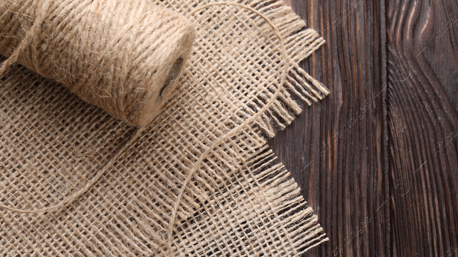 Photo of Spool of thread and burlap fabric on wooden table, closeup. Space for text