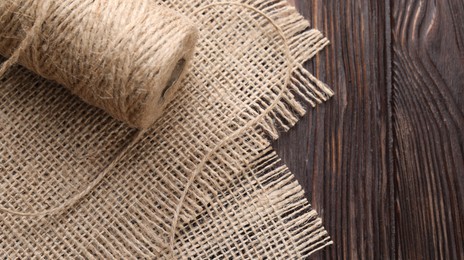 Photo of Spool of thread and burlap fabric on wooden table, closeup. Space for text