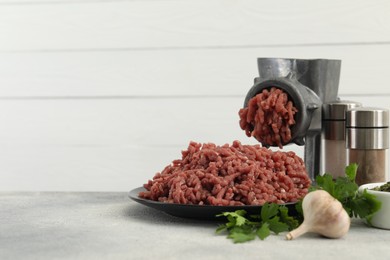 Photo of Mincing beef with manual meat grinder. Parsley, garlic and spices on grey table, space for text