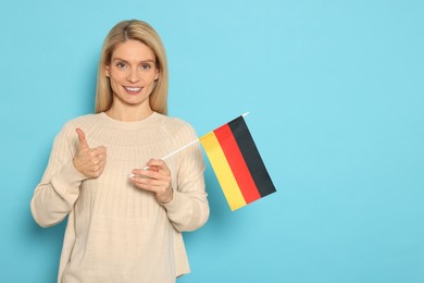 Photo of Woman with flag of Germany showing thumb up on light blue background, space for text
