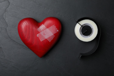 Photo of Red wooden heart and adhesive tape on black stone background, flat lay. Relationship problems concept