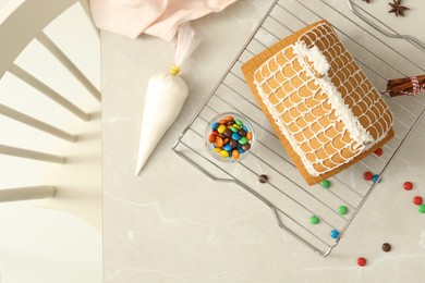 Photo of Gingerbread house with cream on light marble table, flat lay