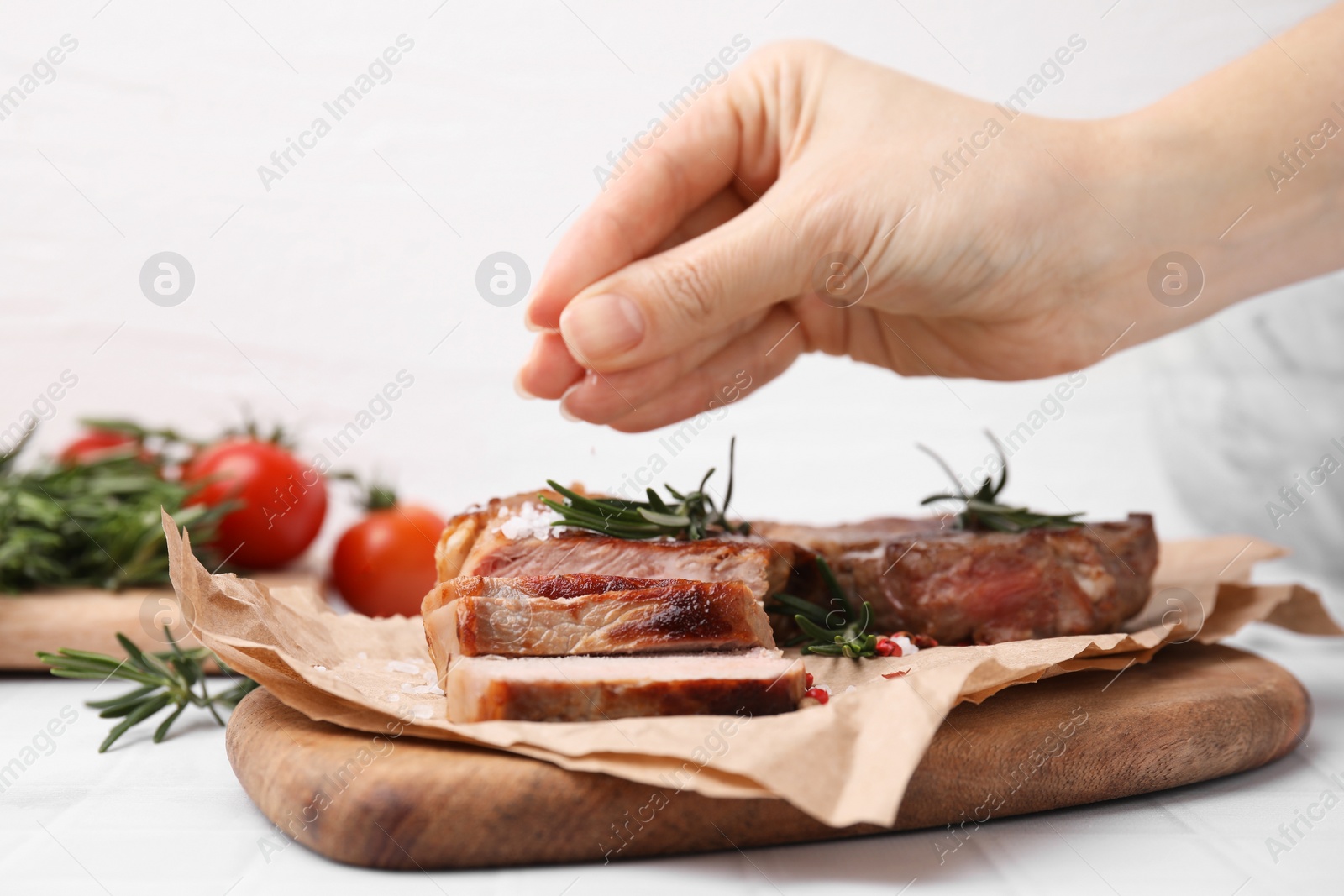 Photo of Woman salting delicious fried meat with rosemary at white table, closeup