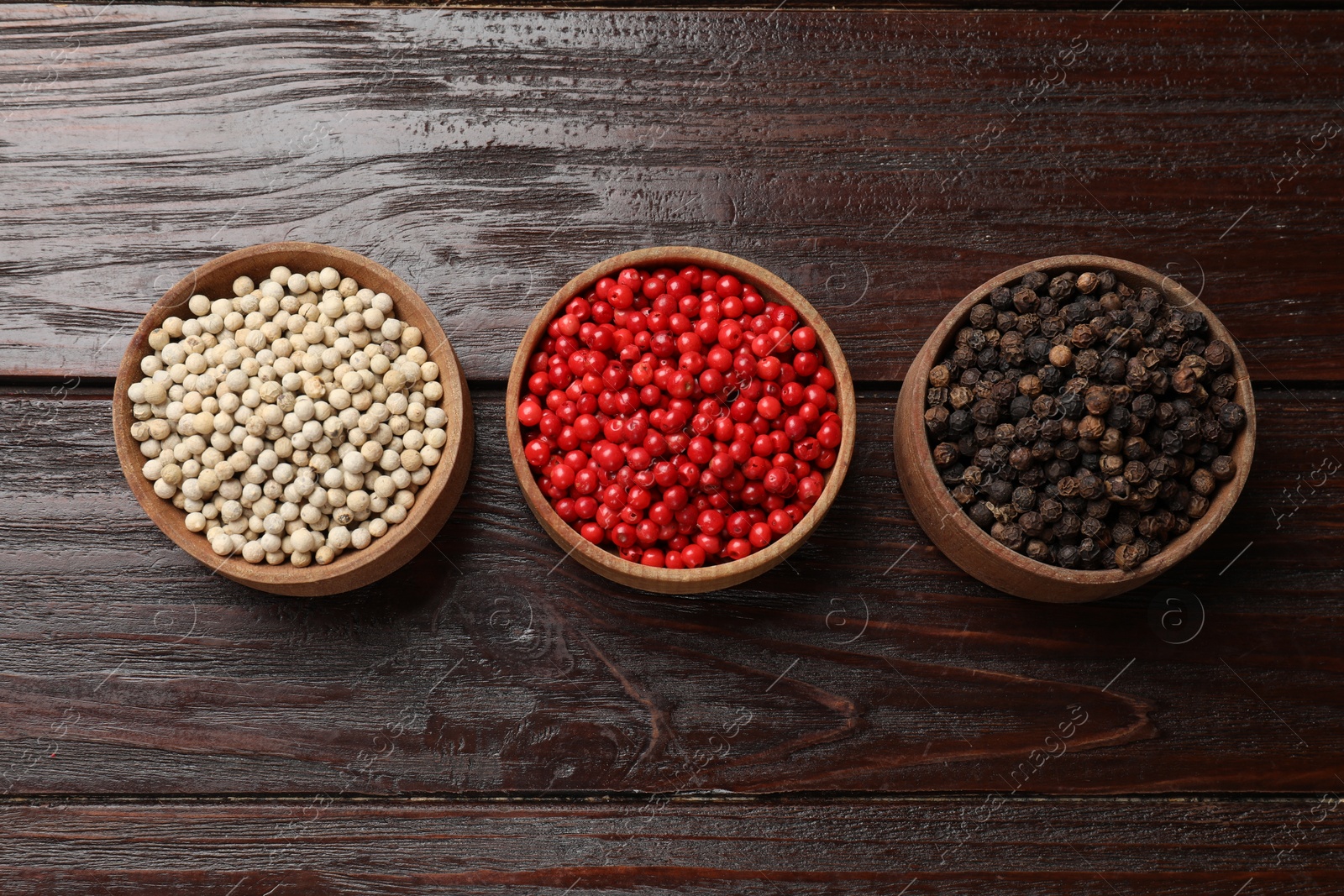 Photo of Aromatic spice. Different peppers in bowls on wooden table, flat lay