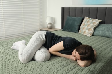 Photo of Sad young woman lying on bed at home