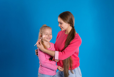 Photo of Happy mother applying powder onto daughter's face on blue background