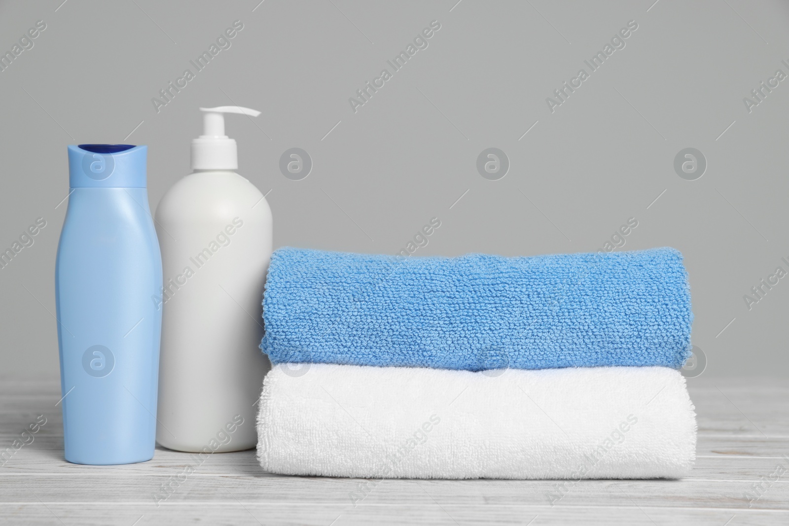 Photo of Soft folded towels with cosmetic products on white wooden table against light grey background