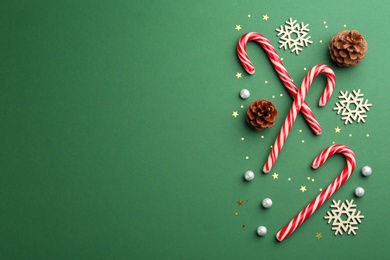 Photo of Flat lay composition with candy canes and Christmas decor on green background. Space for text